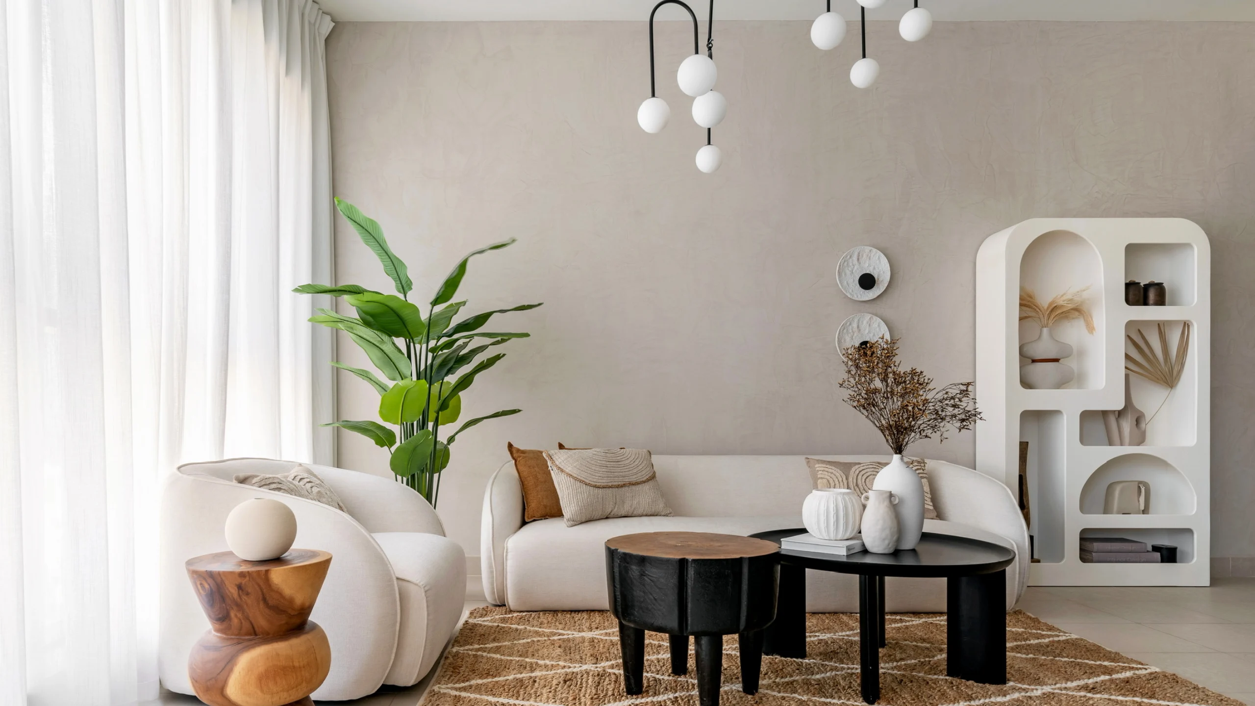 Contemporary living room with curved white sofas, black coffee tables, indoor plants, and earthy neutral interior design.